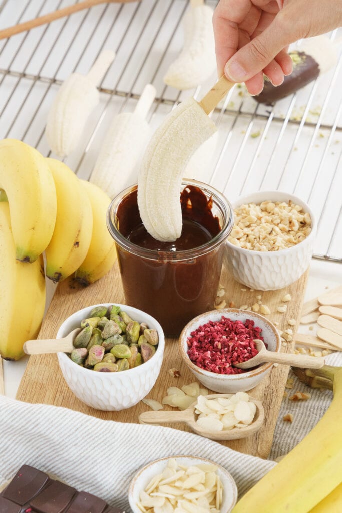hand dipping a banana on a stick in melted chocolate