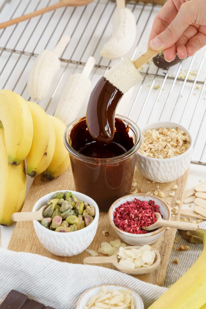 hand dipping a banana on a stick in melted chocolate