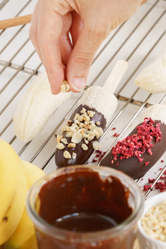 hand sprinkling chopped nuts on frozen chocolate banana