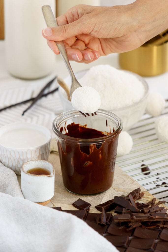 dipping coconut ball into melted chocolate with a fork