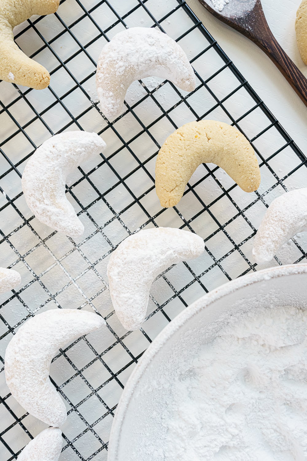 cookies being coated in powdered sugar resting on a cooling rack