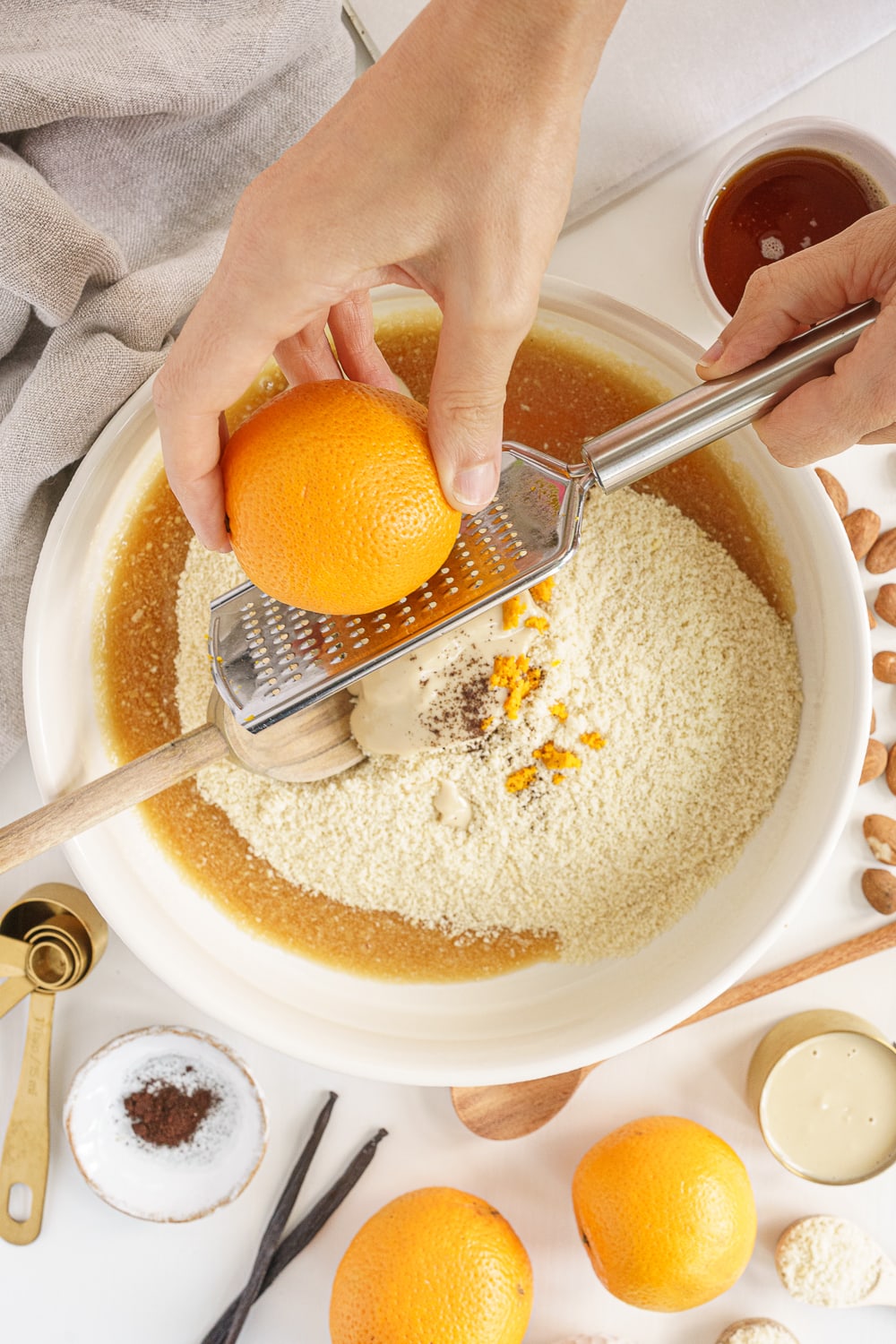 hands zesting an orange on top of a bowl filled with ingredients