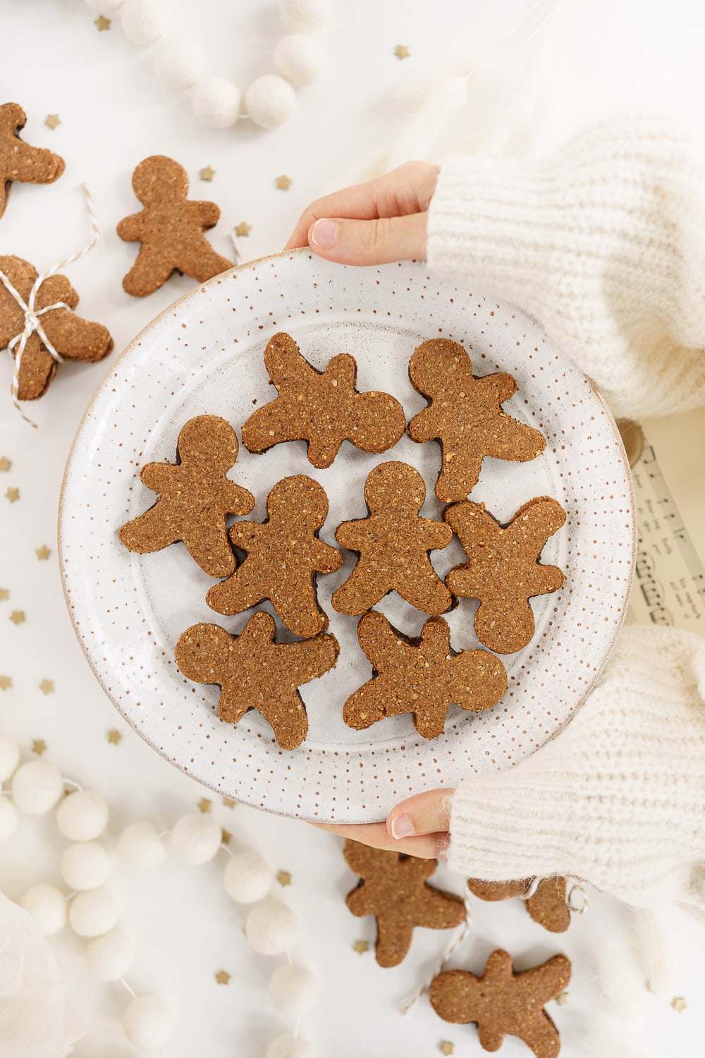 hands holding a plate filled with gingerbread man sandwich cookies
