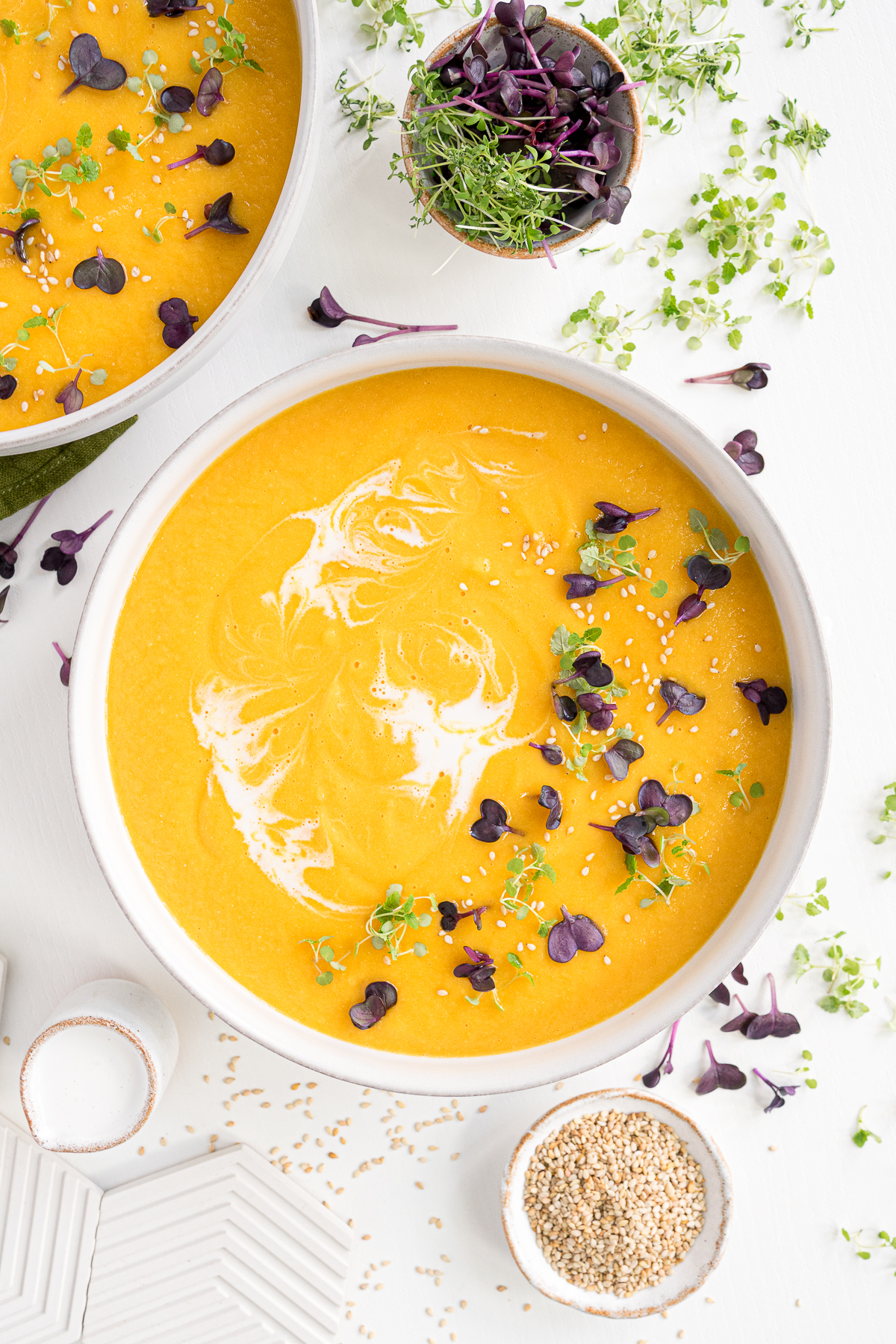Bowl of vegan carrot ginger soup on the table with creamy swirls and microgreens for garnish.