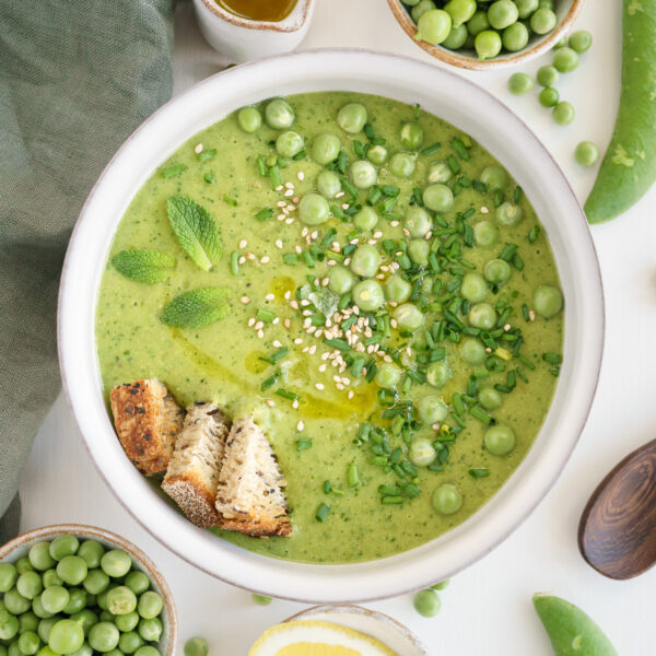 Pureed fresh pea soup in a white bowl with fresh peas, chives and croutons on top.