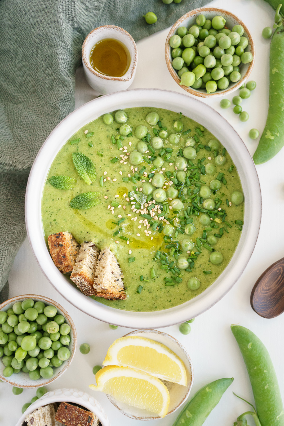 Bowl of fresh pea soup on the table with lemons, whole peas and shelled peas.
