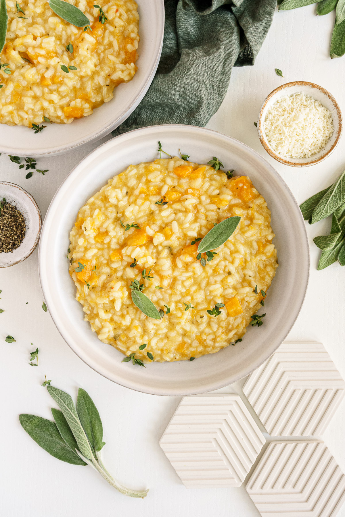 Bowls of butternut squash risotto on the table with parmesan cheese and fresh sage leaves.