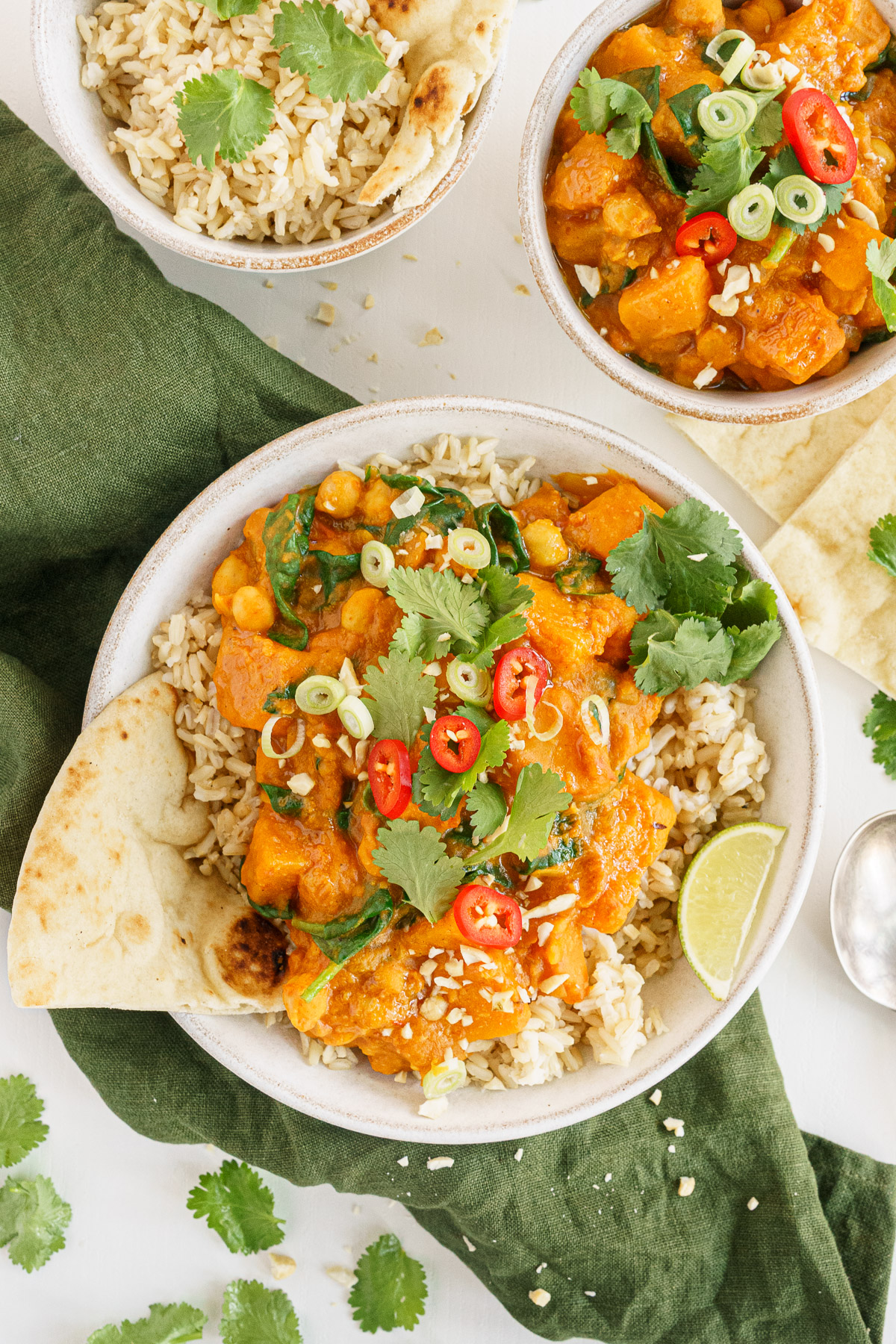 Bowl of butternut squash curry served up on the table with pita and rice.