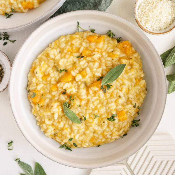 Bowl of butternut squash risotto on the table with side of parmesan cheese.