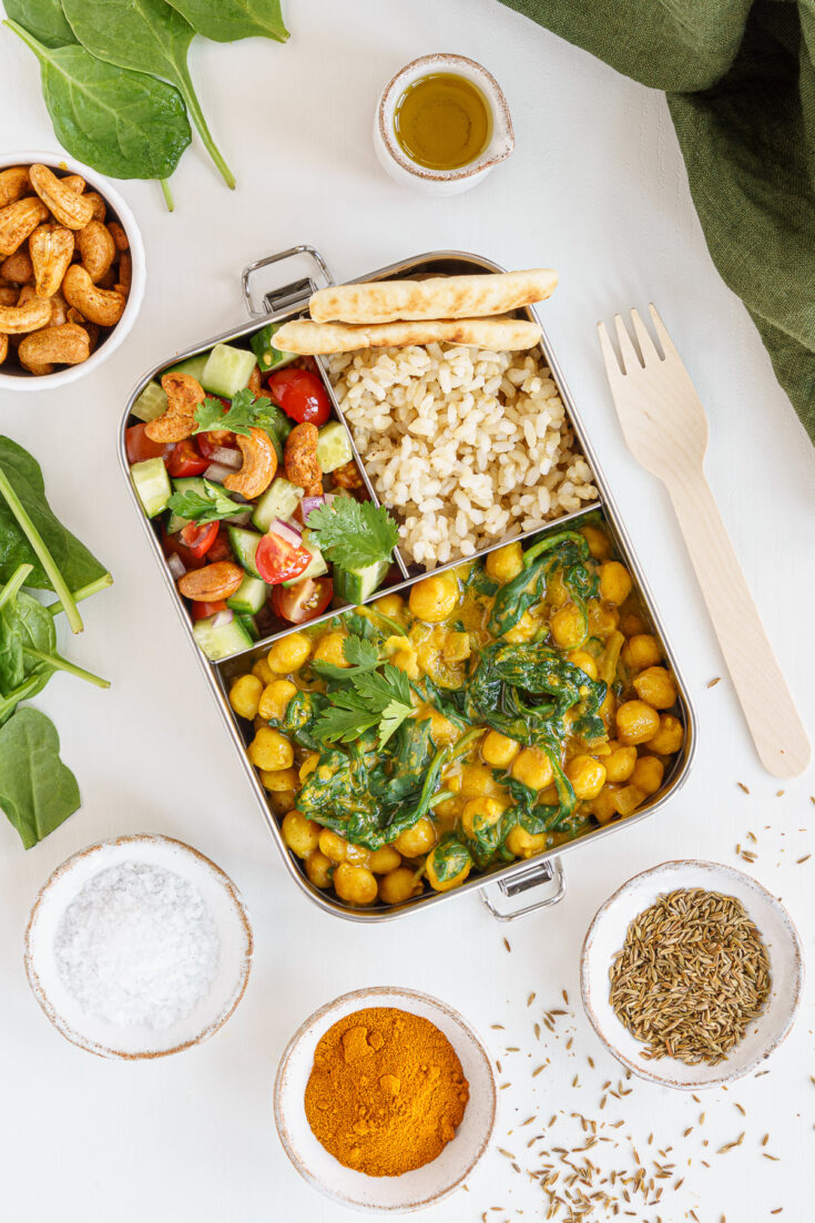 Curry bento box with chickpea curry on the table with naan bread and rice.