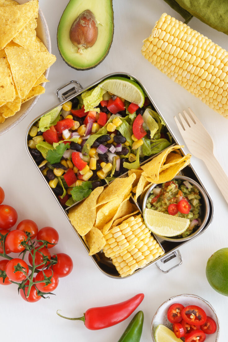 Mexican bento box on the table with corn chips, tomatoes and a fork to carry.
