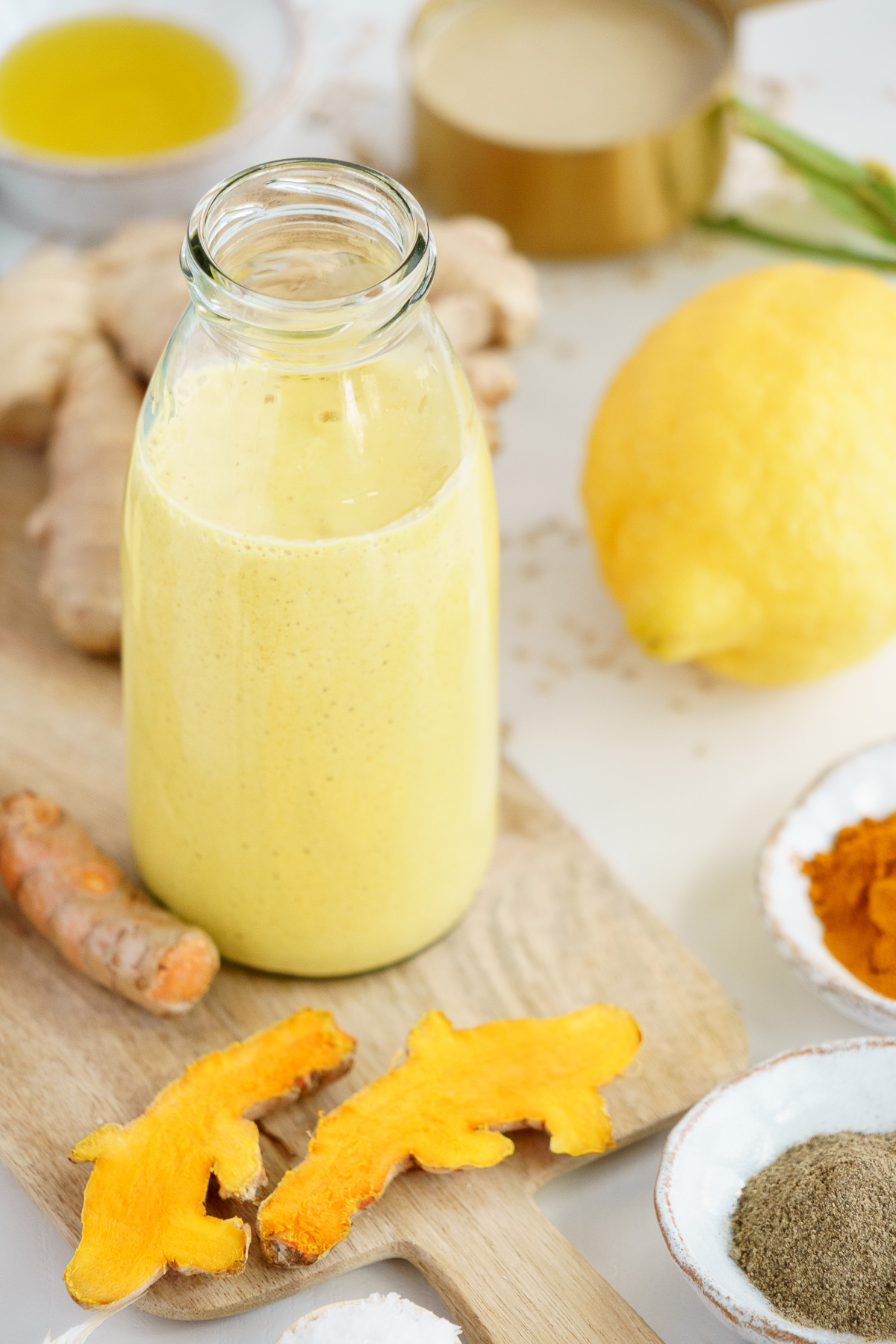 Glass jar filled with turmeric tahini dressing surrounded by ingredients.