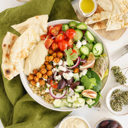 Overhead of hummus bowl on the table with pita bread and olive oil.