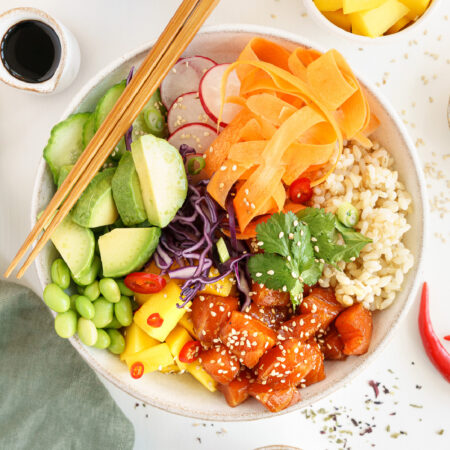 Salmon poke bowl in a white dish with chopsticks laying on the edges of the bowl.
