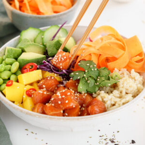 Salmon poke bowl on the table with chopsticks digging in.