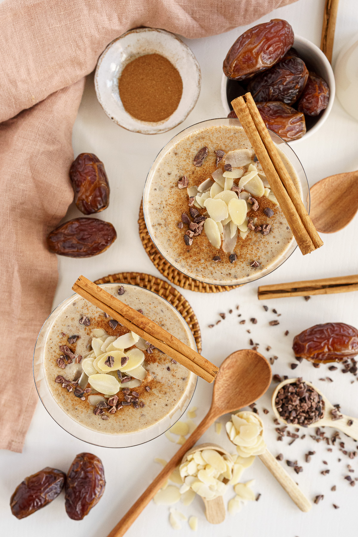 Overhead of date smoothies garnished with cinnamon sticks, almonds and cacao nibs.
