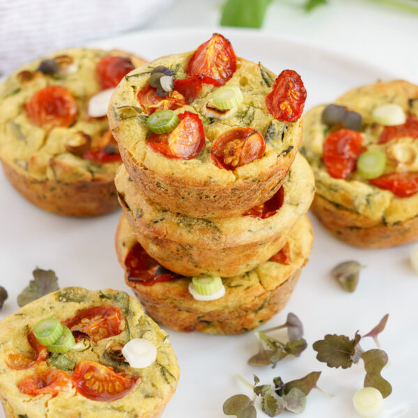 Three vegan egg muffins in a stack with more around it garnished with fresh herbs.