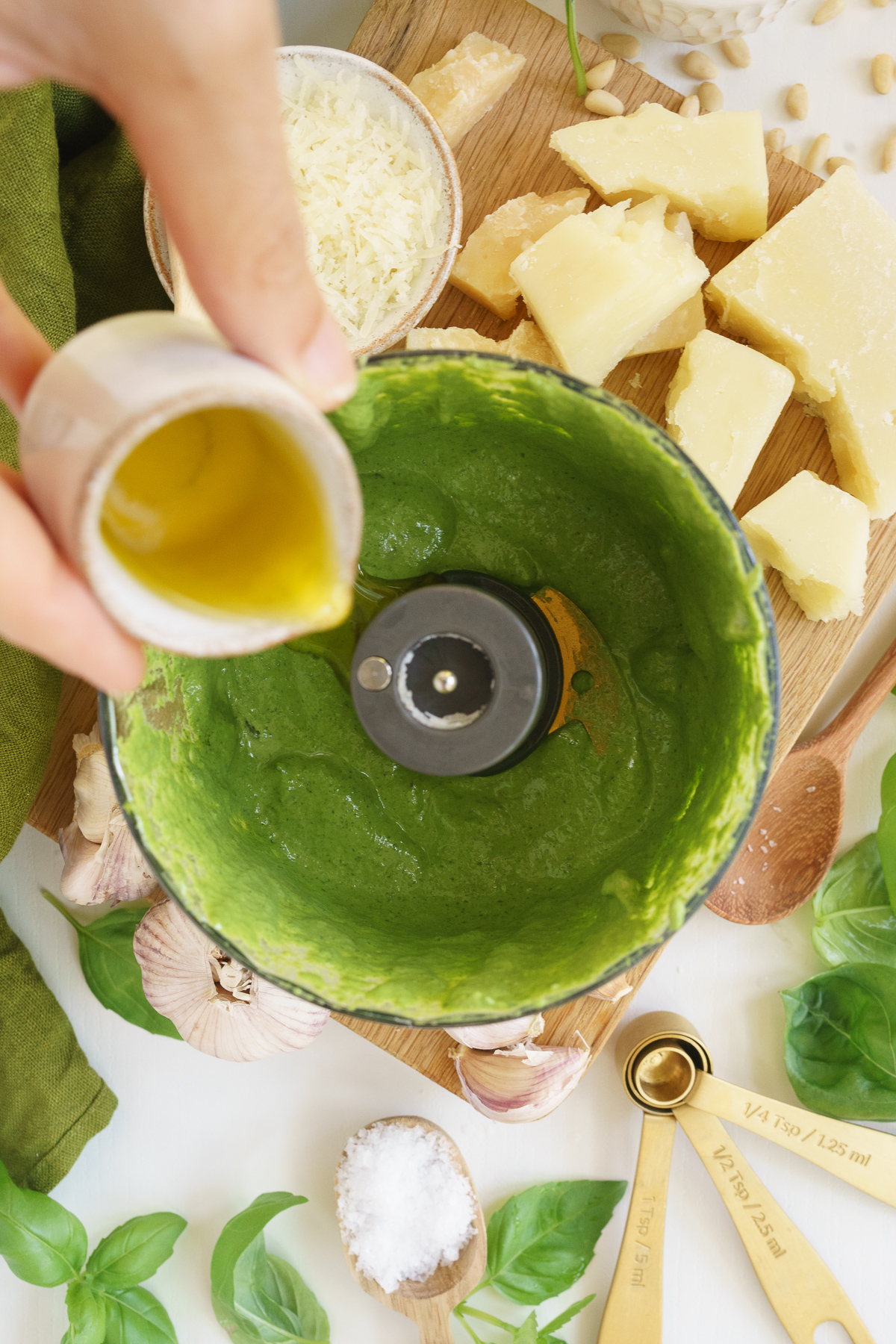 Adding olive oil to the basil pesto in the food processor.