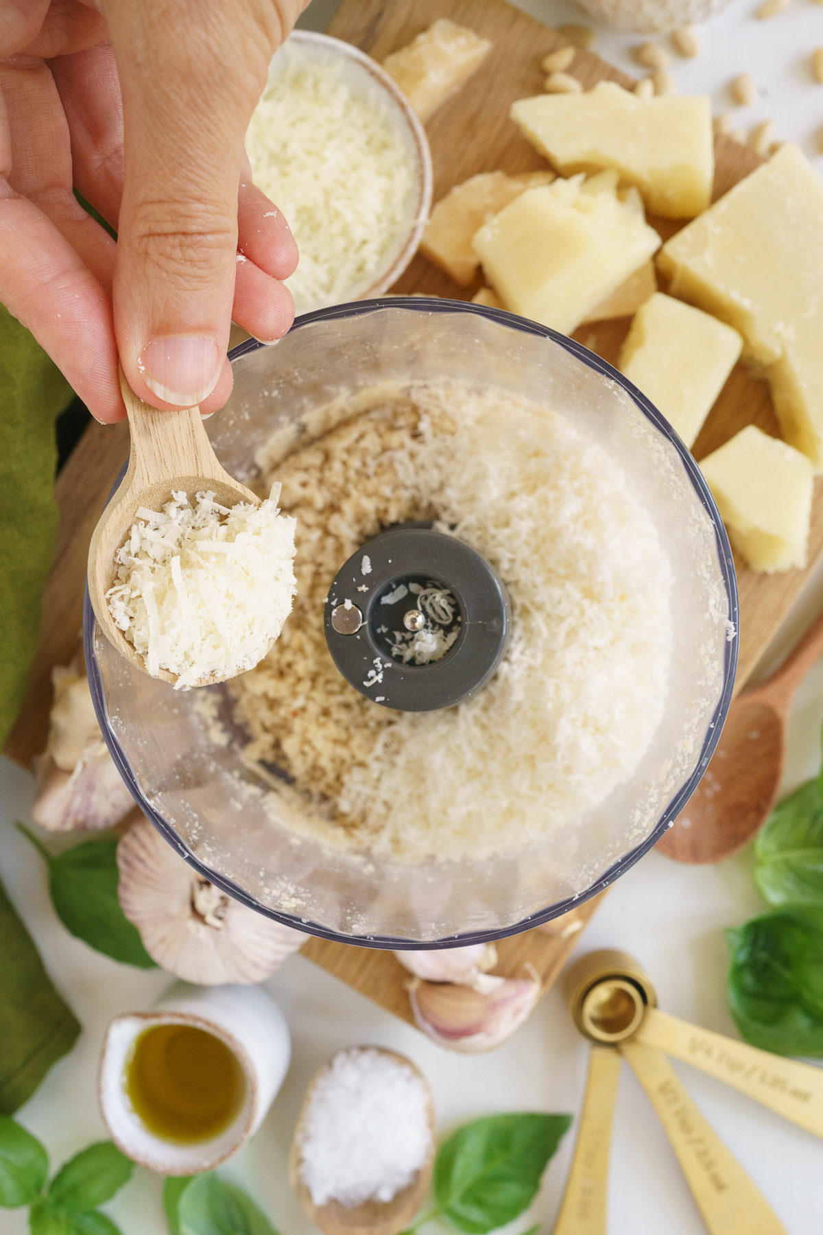 Adding the cheese to the food processor to make basil pesto.