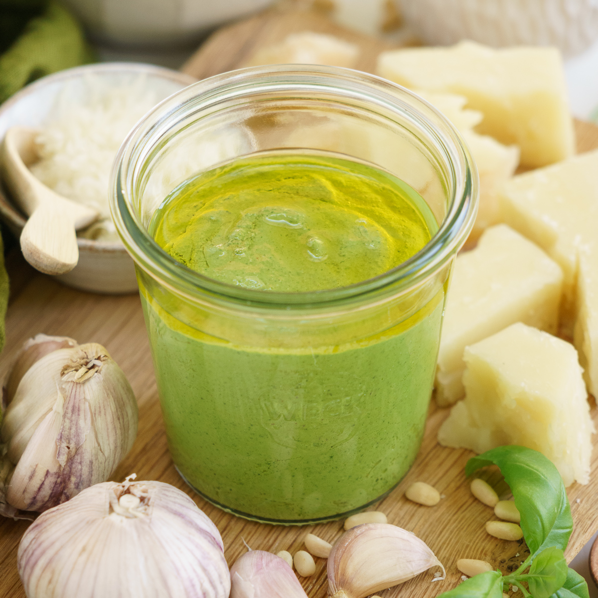 Jelly jar filled with genovese pesto on the table with ingredients around it.