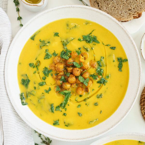 A white bowl filled with yellow turmeric chickpea soup on the table with green garnish and chickpeas on top.