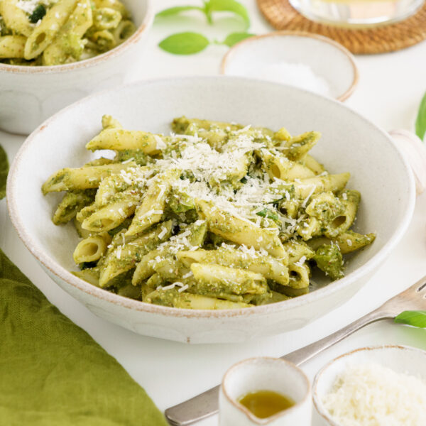 Zucchini pesto pasta in a white bowl with a bowl of parmesan cheese on the table.