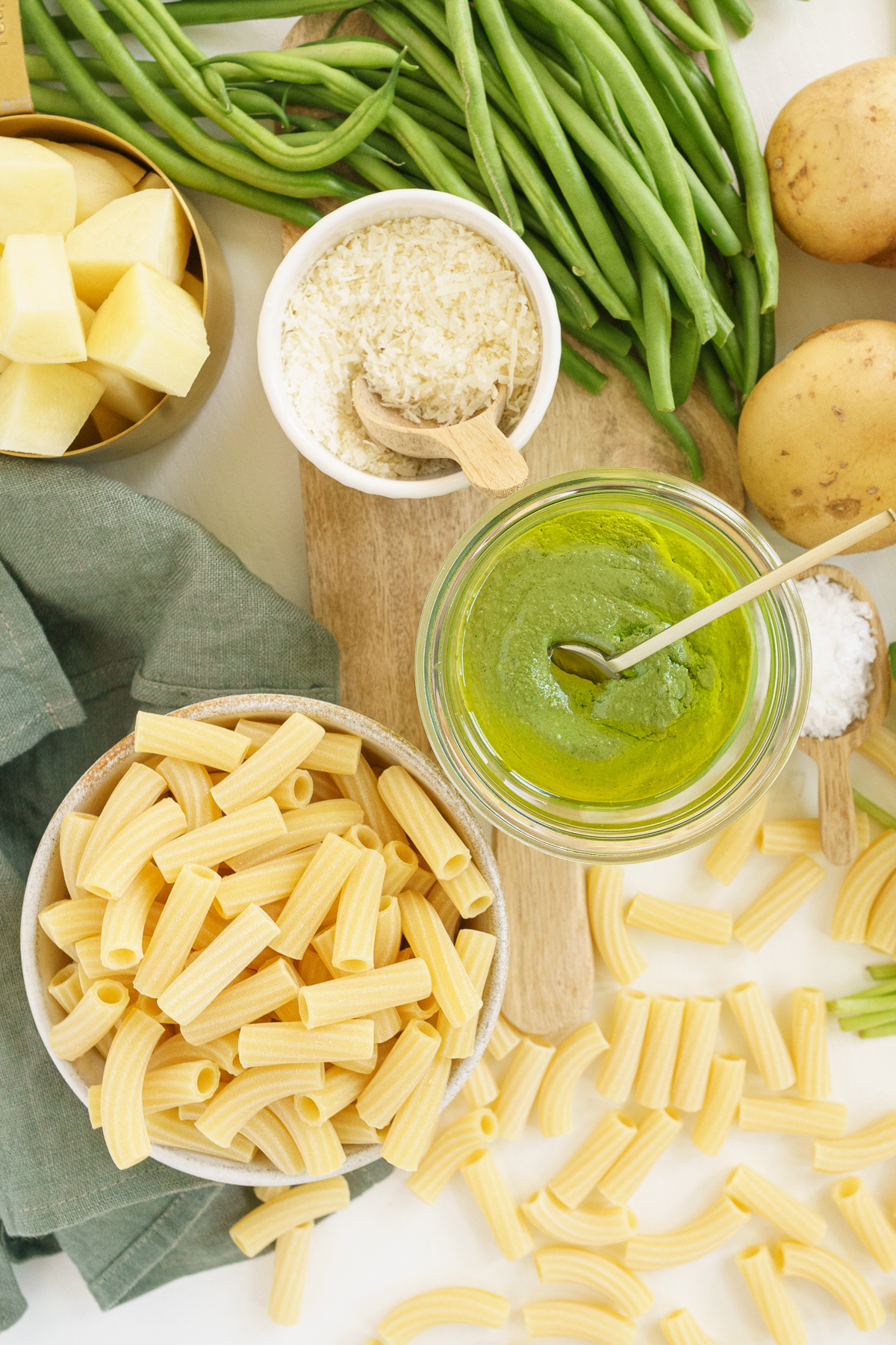 Top view of raw pasta, cheese, salt, potato, basil pesto sauce, and green beans