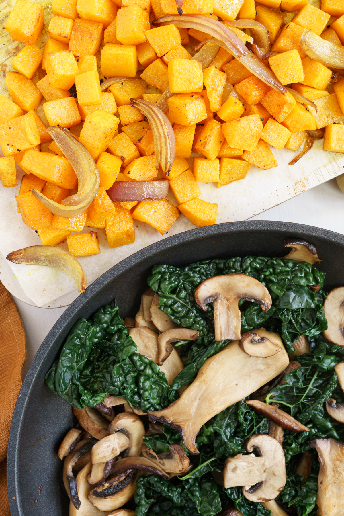 Cooked butternut squash on a pan and cooked kale and mushrooms in a pan.