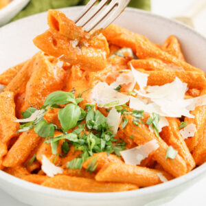 Close up of a fork digging into roasted red pepper pasta in a bowl