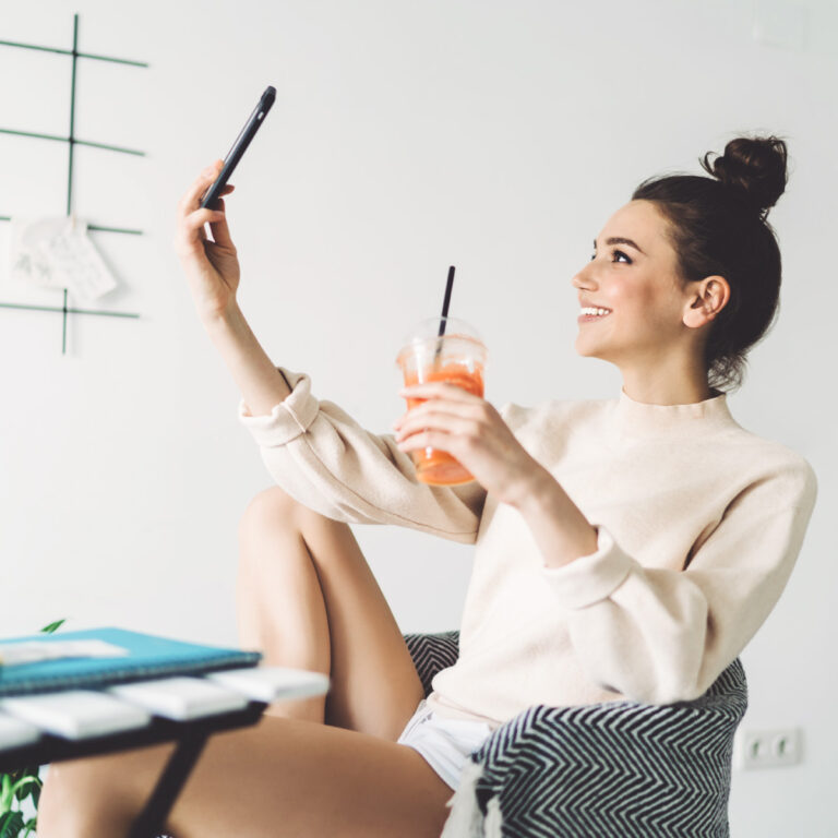 Smiling woman taking a TikTok video with smartphone while sitting in a chair