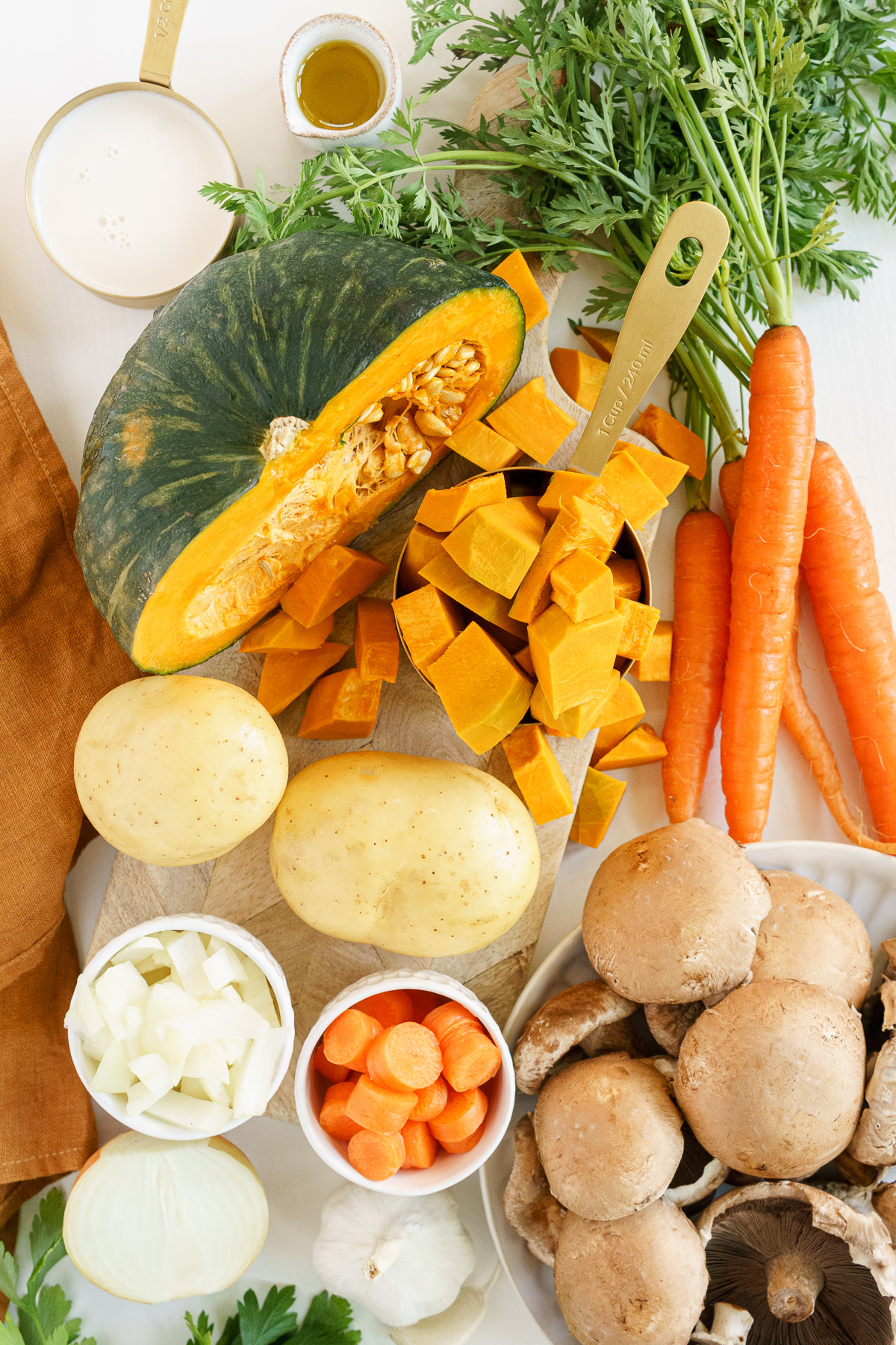 pumpkin soup ingredients in the table. pumpkin, carrots, potatoes, almond milk, onions, olive oil, fresh parsley
