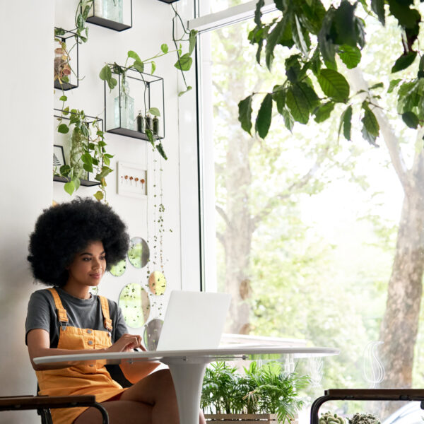 Black woman working on her laptop in a coffee shop full of plants
