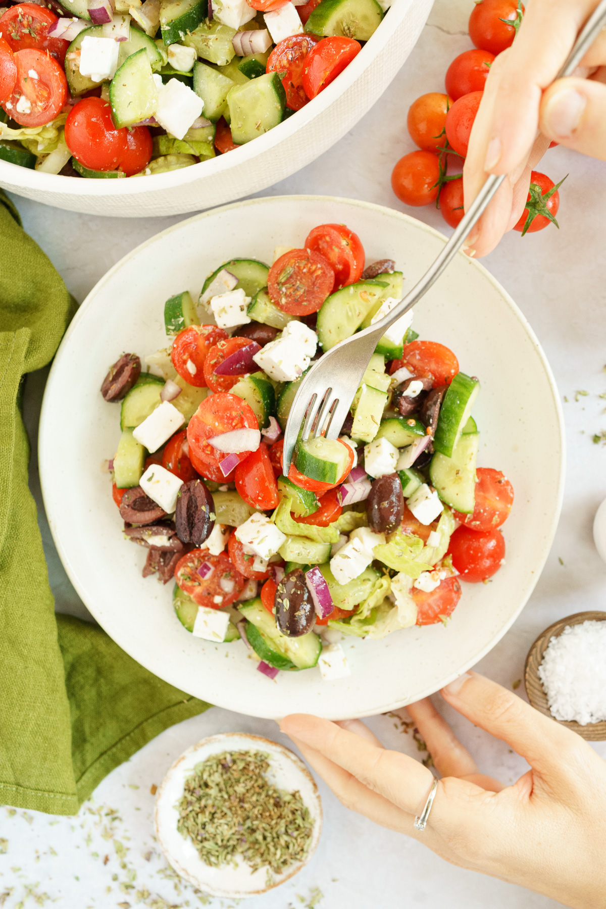Hand holding a plate of Greek salad with a fork