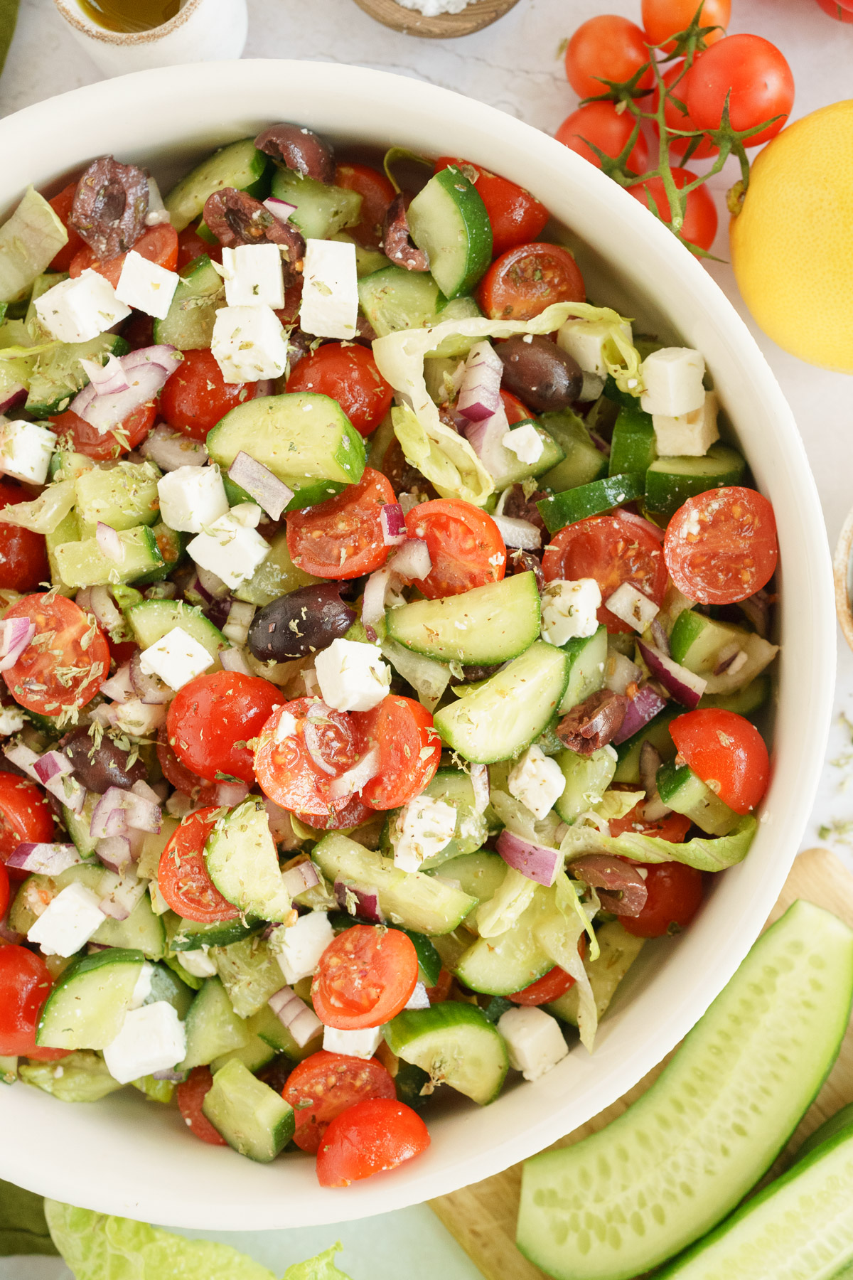 Partially cropped bowl of Greek salad, featuring fresh lettuce, cucumbers, tomatoes, red onions, feta cheese, and Kalamata olives, 