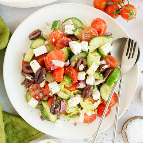 Top view of a mouth-watering Greek salad with lettuce on a plate with utensils beside it.