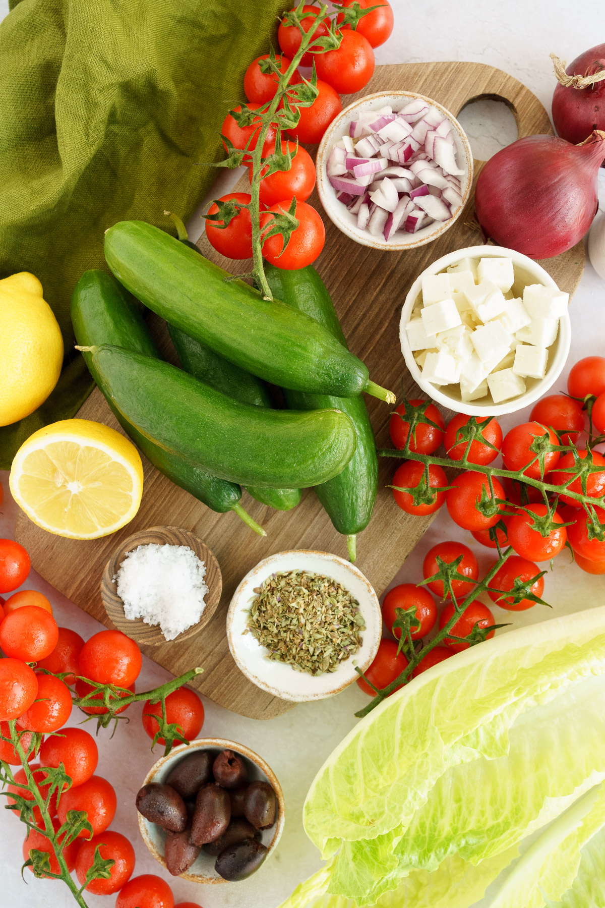 Fresh and colorful ingredients for Greek salad with lettuce displayed on a table, including tomatoes, cucumbers, onions, feta cheese, olives, and lettuce leaves.