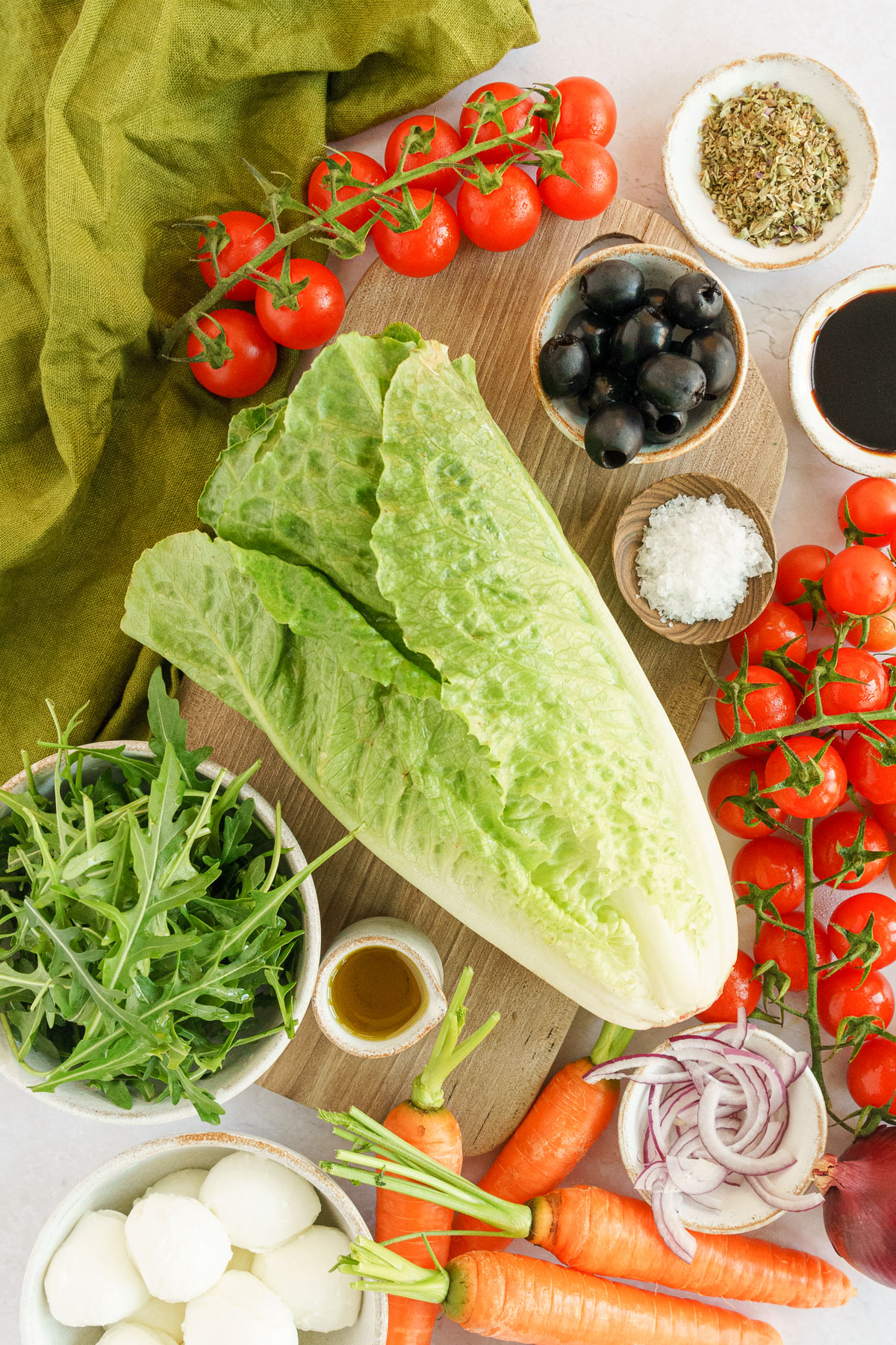 italian salad ingredients lettuce,tomatoes, black olives, carrots, onions anda arugula leaves on top of the table