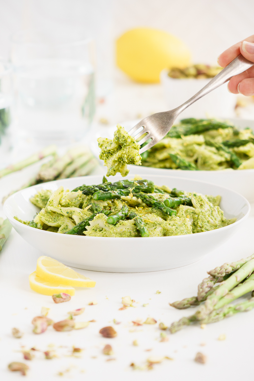 close up of hands picking up some asparagus pasta with a fork from a plate