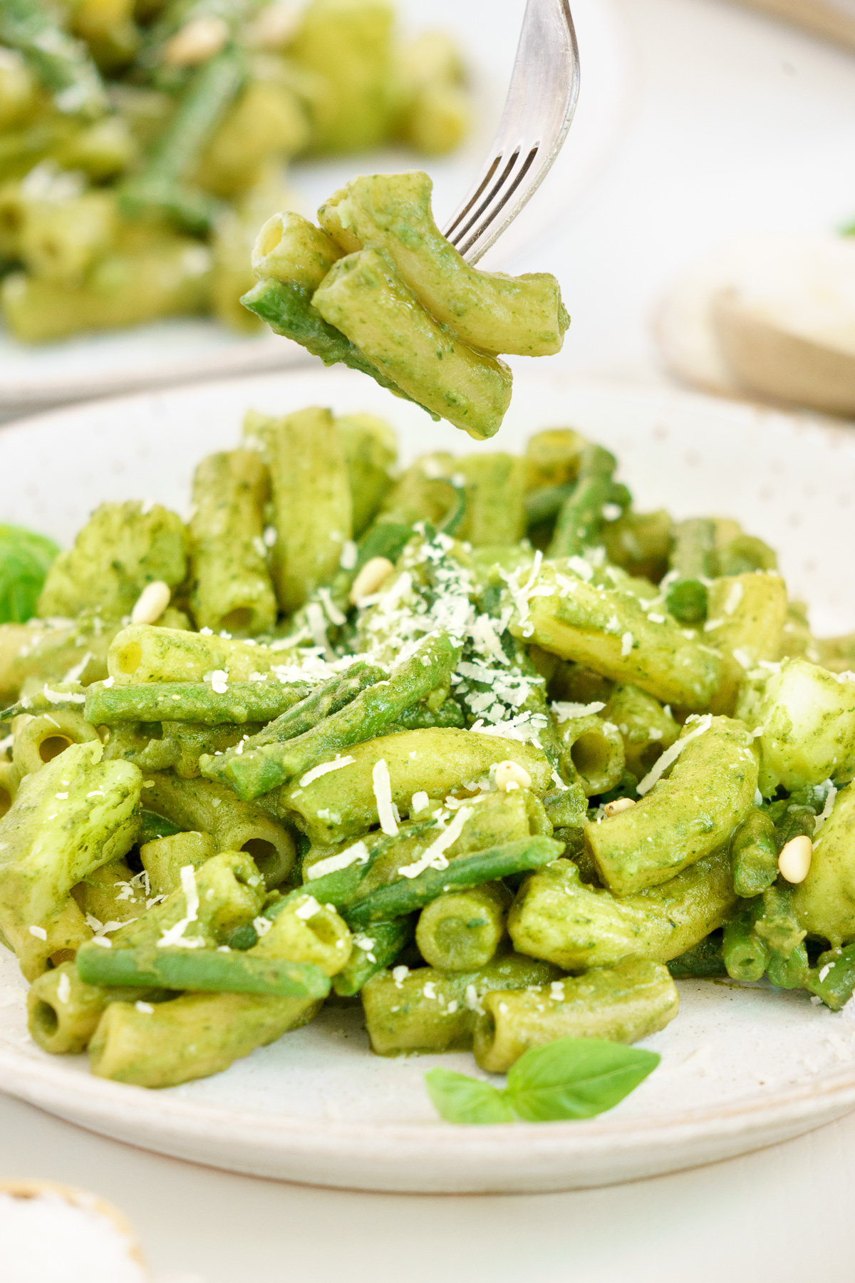 Close up view of a fork and full plate of basil pesto pasta 