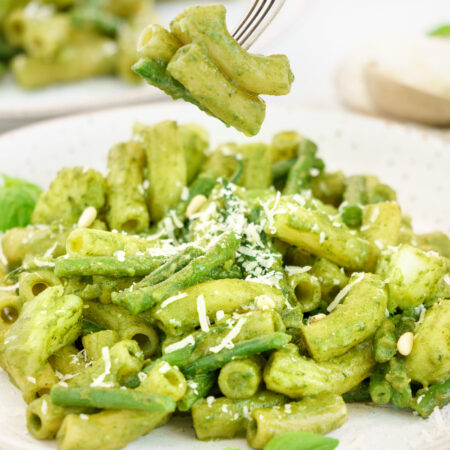 Fork picking up basil pesto pasta from a plate