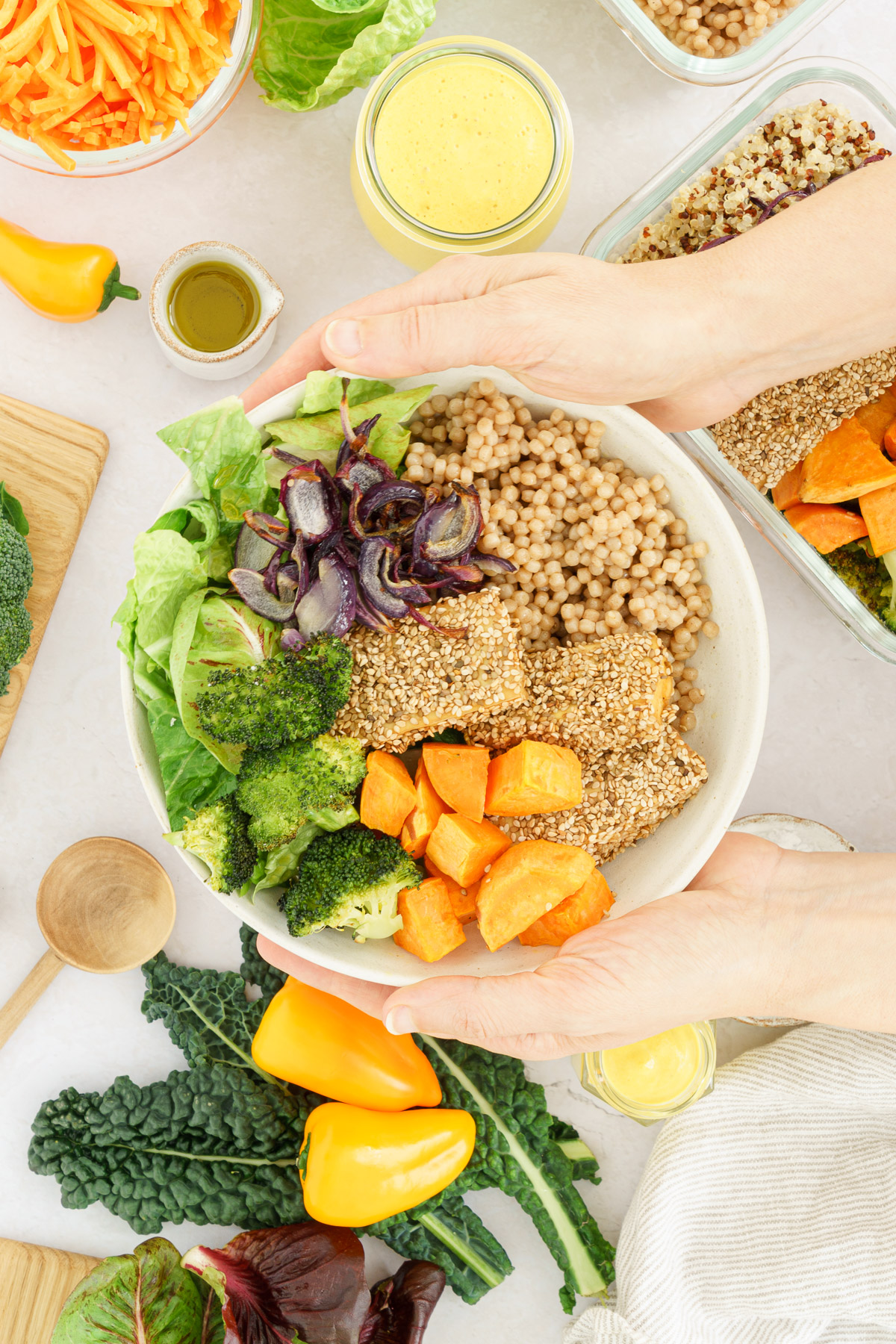 Hands holding a bowl filled with couscous, roasted veggies and tofu