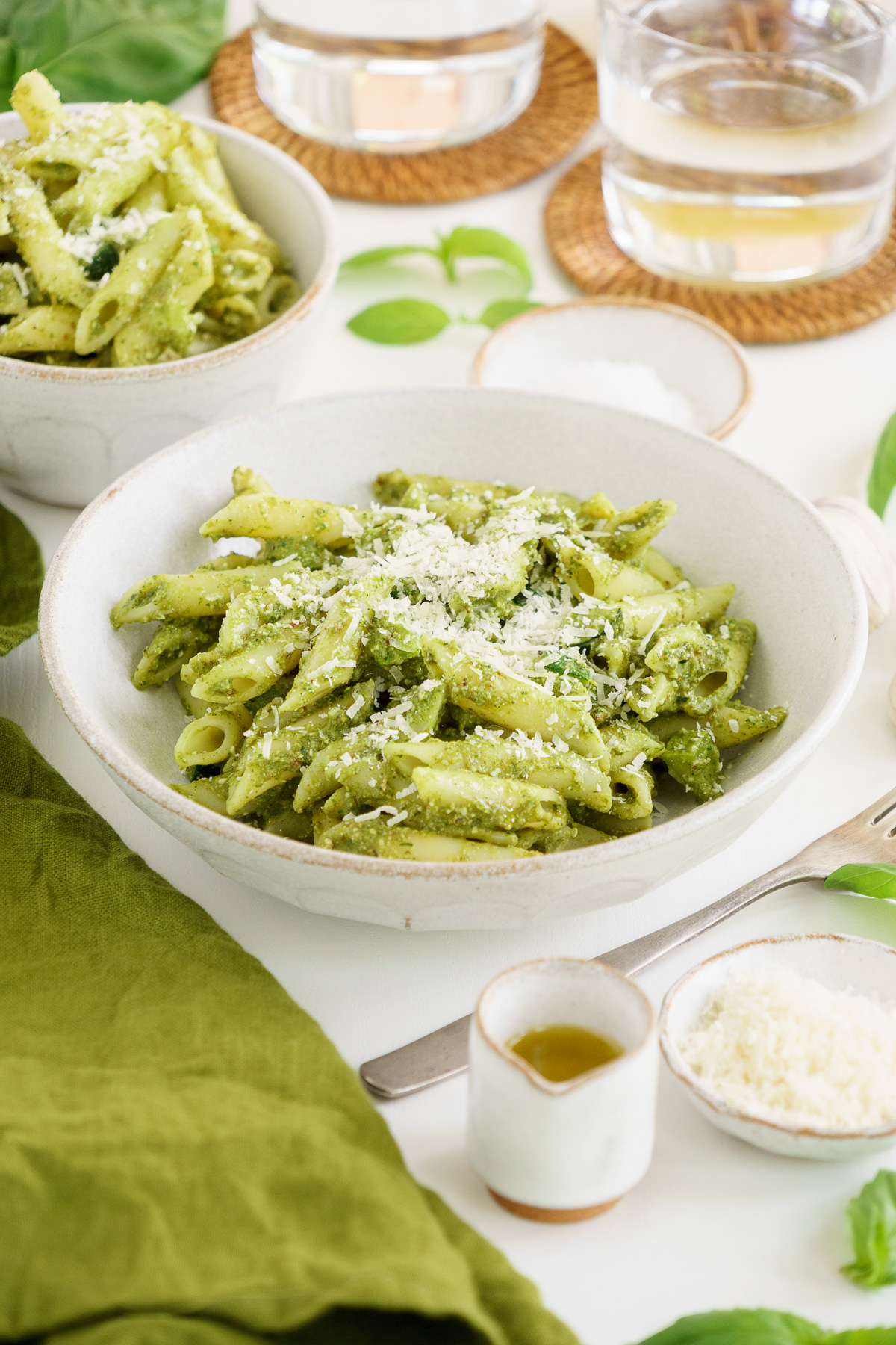 Bowl of zucchini pesto penne pasta on the table with parmesan cheese.