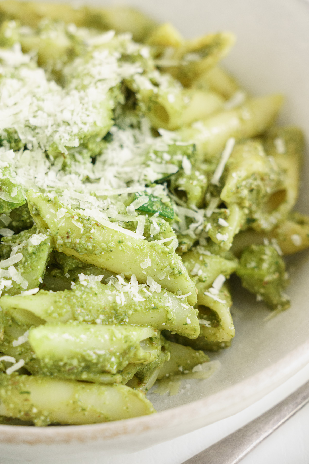 Close up of bowl filled with zucchini pesto pasta with parmesan cheese on top.