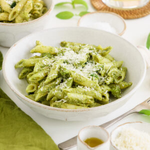 Bowl of zucchini pesto penne pasta on the table with parmesan cheese.