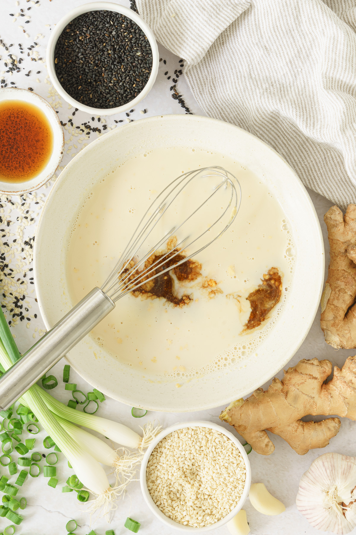 top view of a whisk and a bowl of the dipping sauce with soy sauce added, and rice vinegar, ginger, green onions, and white and black sesame seeds
