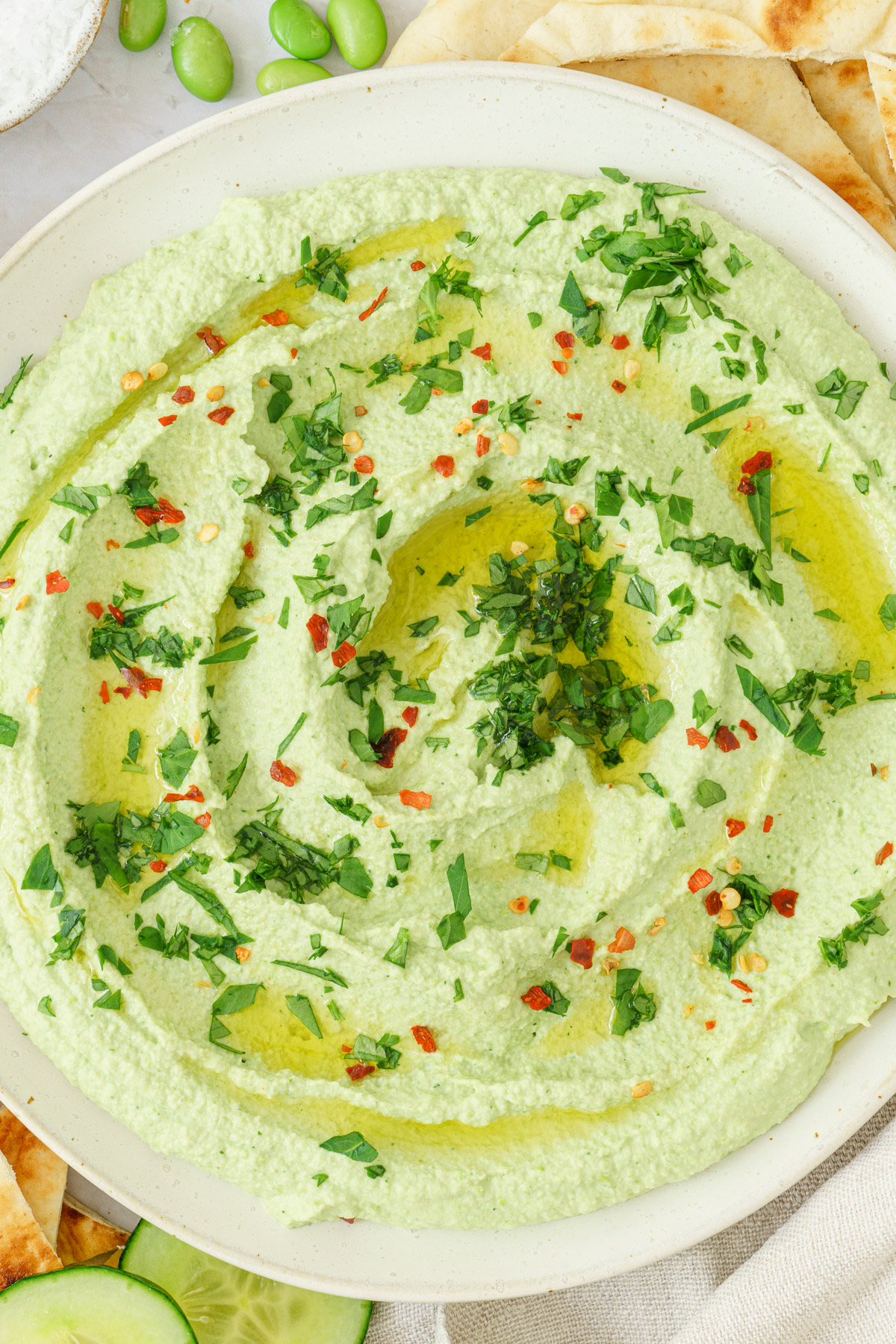 close up image of an edamame hummus sprinkled with herbs and chili flakes
