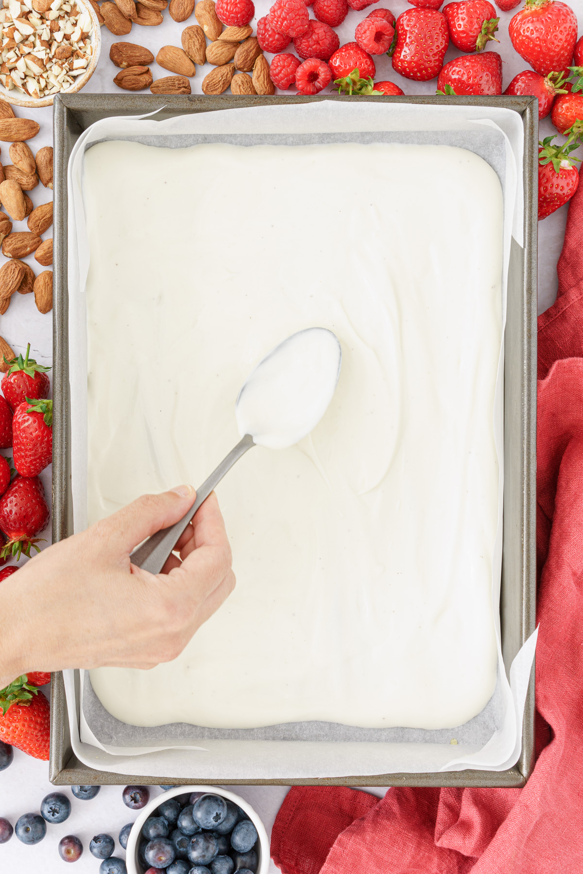 top view image of a hand spreading greek yogurt mixture into the baking sheet