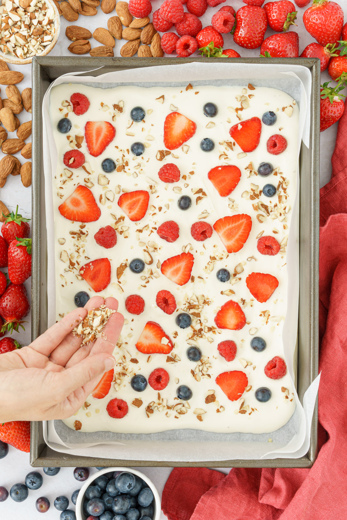 a hand sprinkling nuts on top of the yogurt and berries mixture