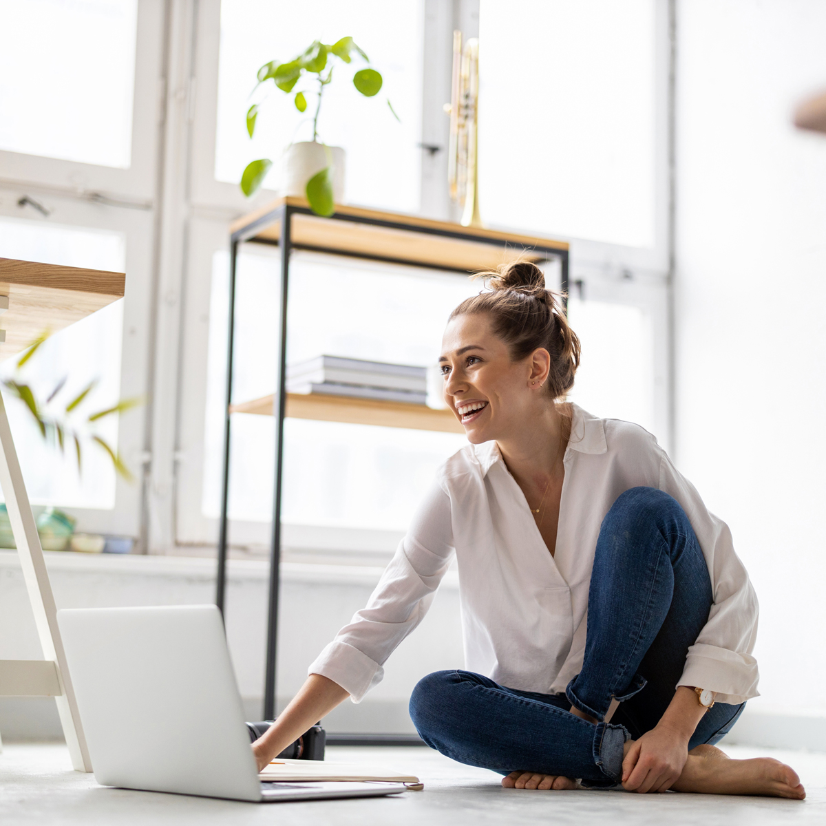 Woman sitting on the floor smiling while working at her laptop