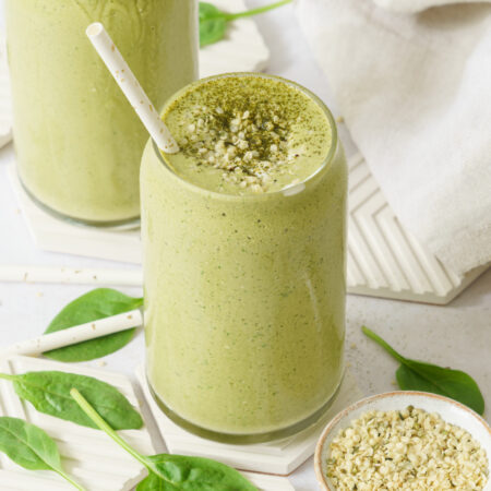 close up image of a glass full of matcha smoothie top with hemp seeds with straw